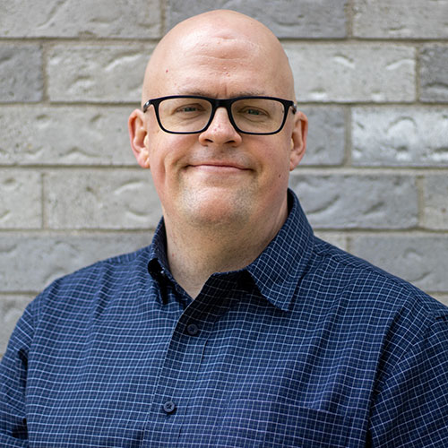 headshot of Colin with a brick wall in the background
